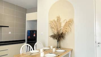 Een eethoek met een houten tafel, witte stoelen en een vaas met pampa's.
