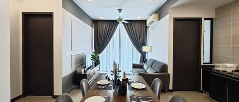 A modern dining area with a wooden table set for four, flanked by dark sofas and a kitchen area.