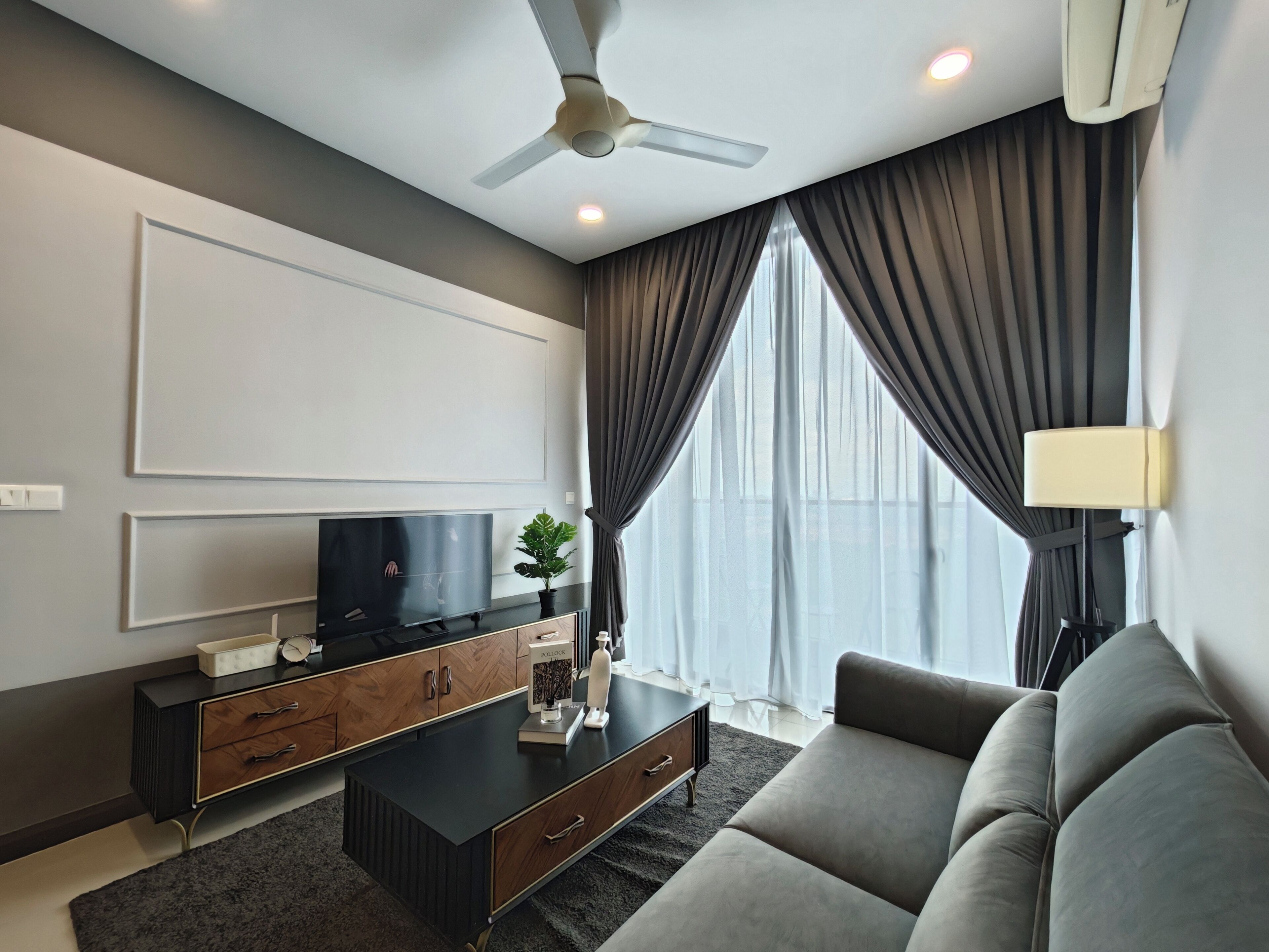 Ein modernes Wohnzimmer mit Flachbildfernseher, einer Couch, einem Couchtisch und einem Deckenventilator.