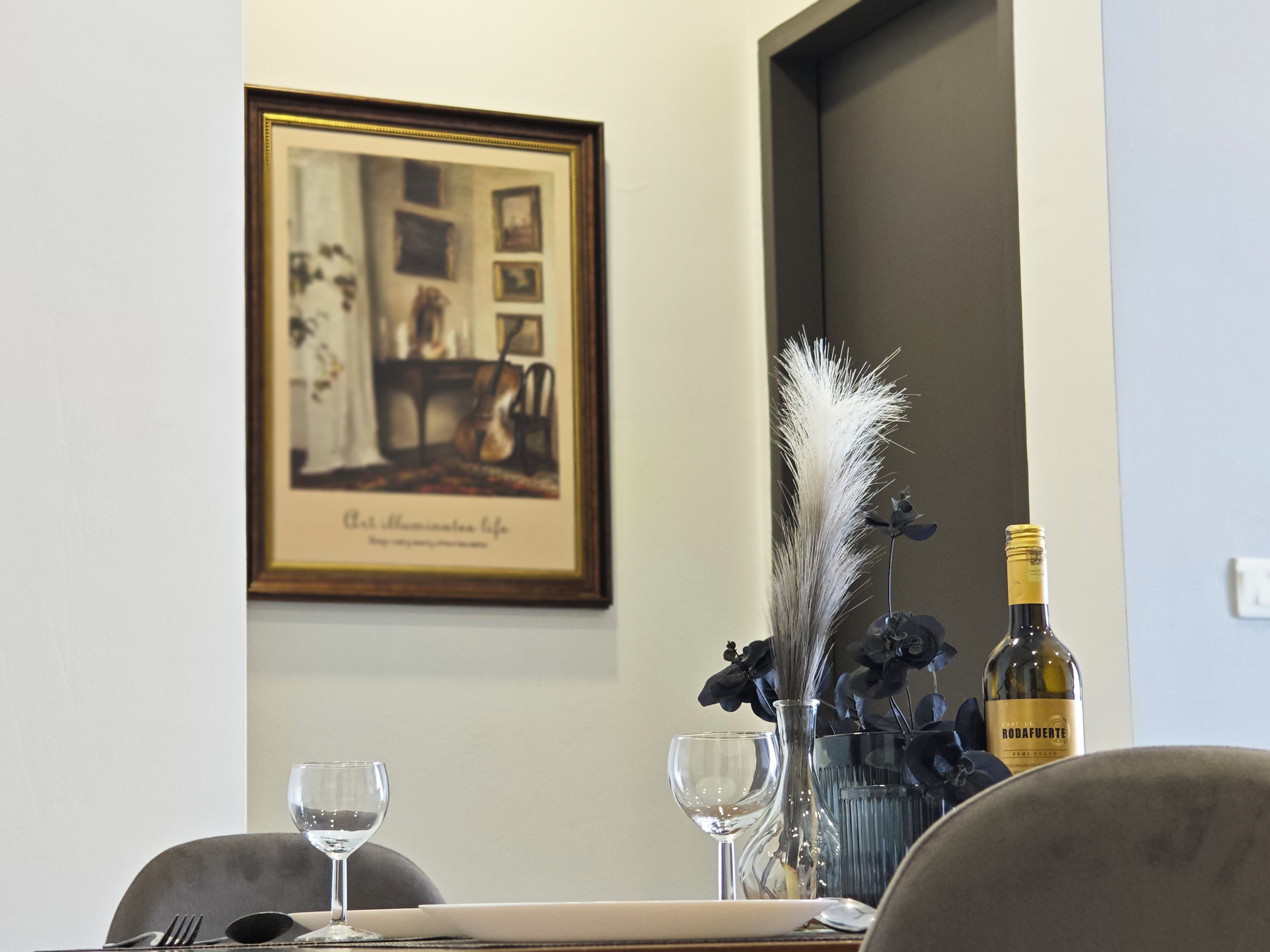 A dining table with two wine glasses, a bottle of wine, and a vase with dried flowers.