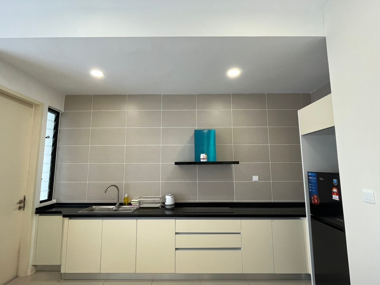 Una cocina moderna con encimera negra, armarios blancos y un electrodoméstico verde azulado sobre una estantería negra.