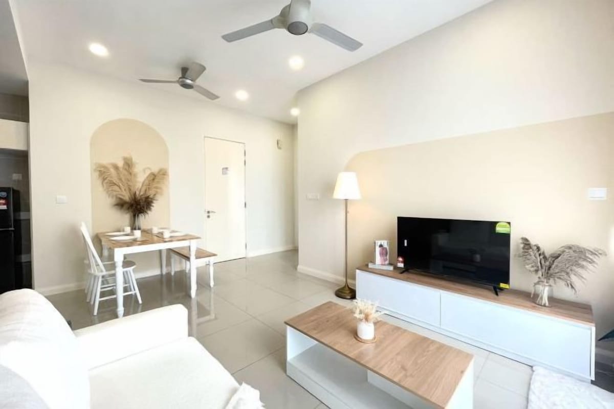 A modern living room with a flat-screen TV, white sofas, a wooden coffee table, and a dining area with a white table and chairs.