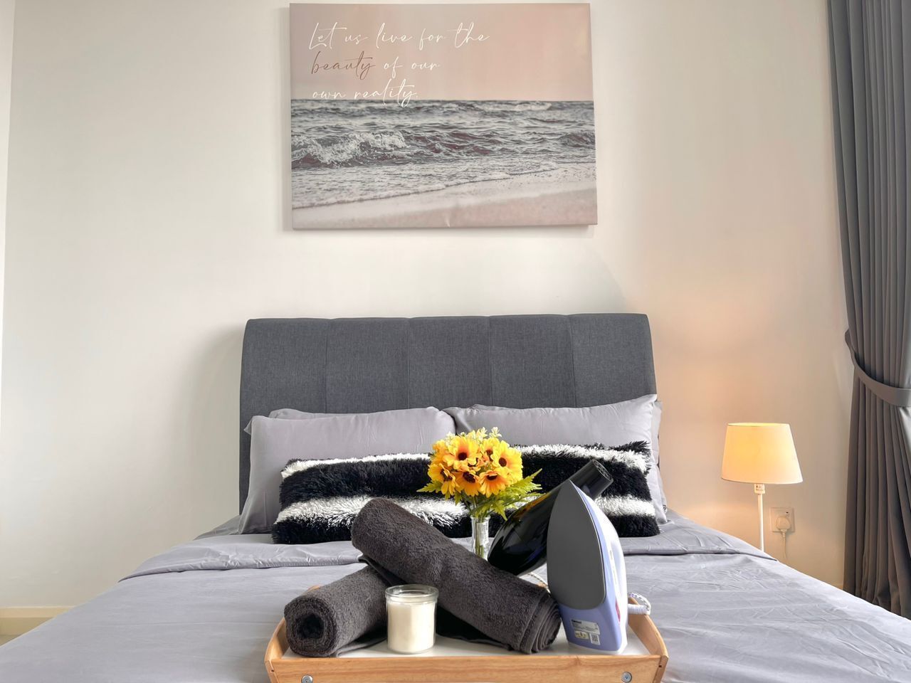 Un lit bien fait, avec une tête de lit grise, une lampe de chevet et une citation encadrée accrochée au mur.