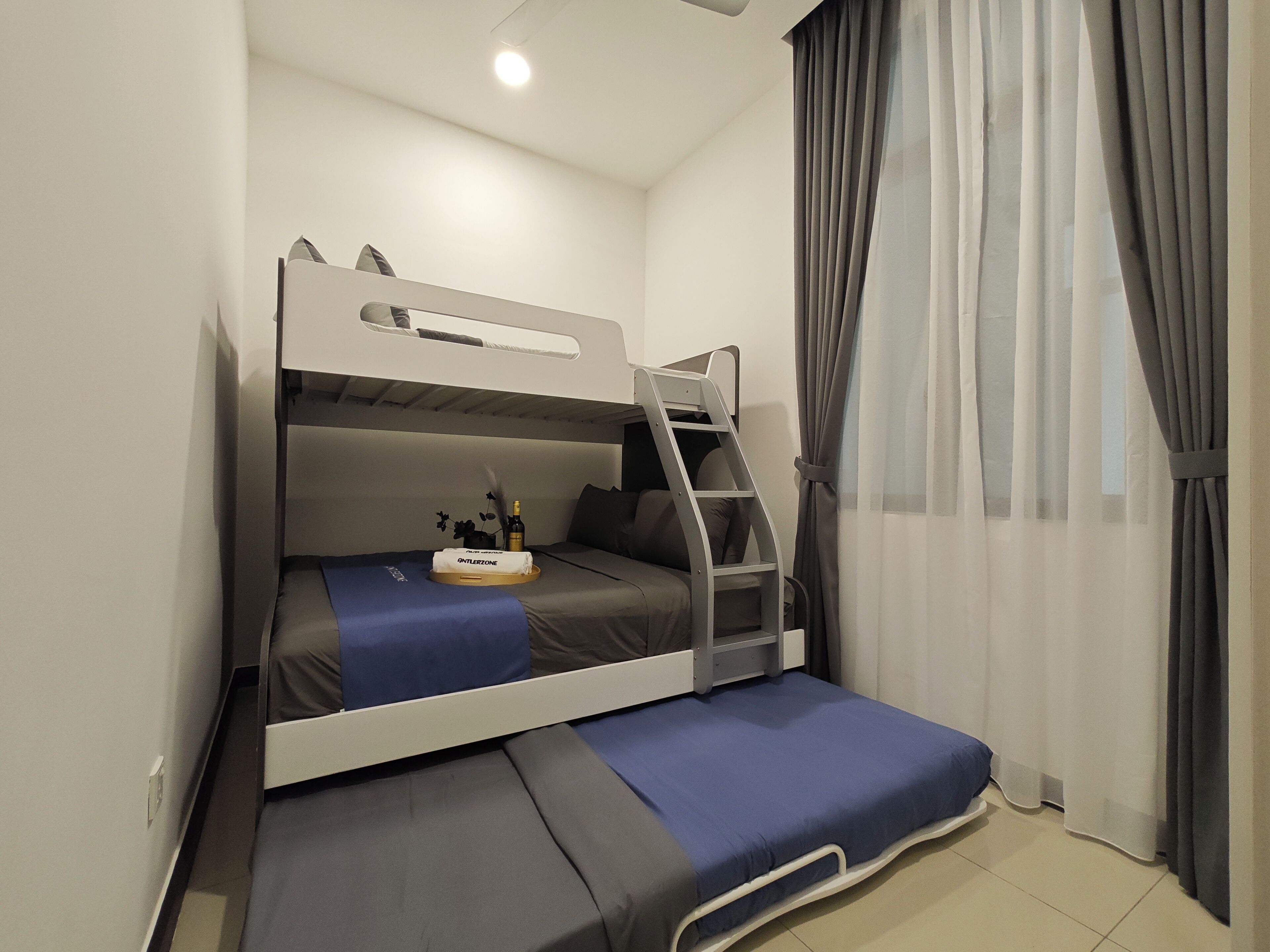 A bunk bed room with a ladder, a small table with a bottle and a towel, and a window with curtains.