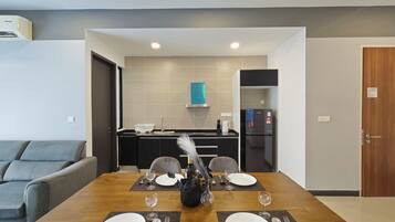 A modern dining room with a wooden table set for four, a kitchen in the background, and a grey sofa.