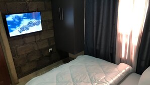 Ein Hotelzimmer mit Bett, Fernseher an einer Ziegelwand, Kleiderschrank und einem Fenster mit Vorhängen.