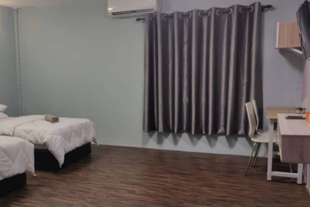 A room with two beds, a desk, a chair, a wall-mounted fan, and a curtain.