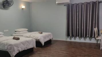 Ein Zimmer mit zwei Betten, einem Schreibtisch, einem Stuhl, einem Wandventilator und einem Vorhang.