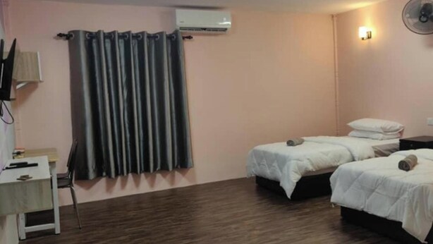 A room with two single beds, a desk, an air conditioner, and a wall-mounted fan.