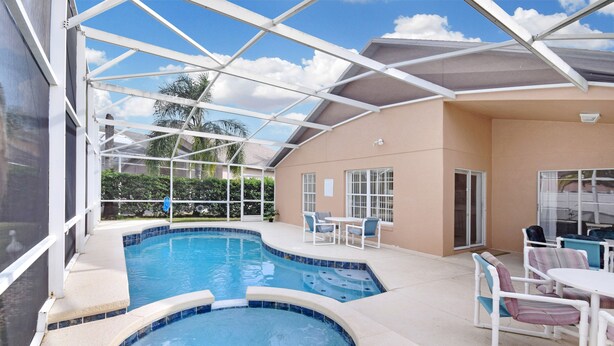 A covered outdoor swimming pool area with a hot tub, patio furniture, and a view of the surrounding landscape.