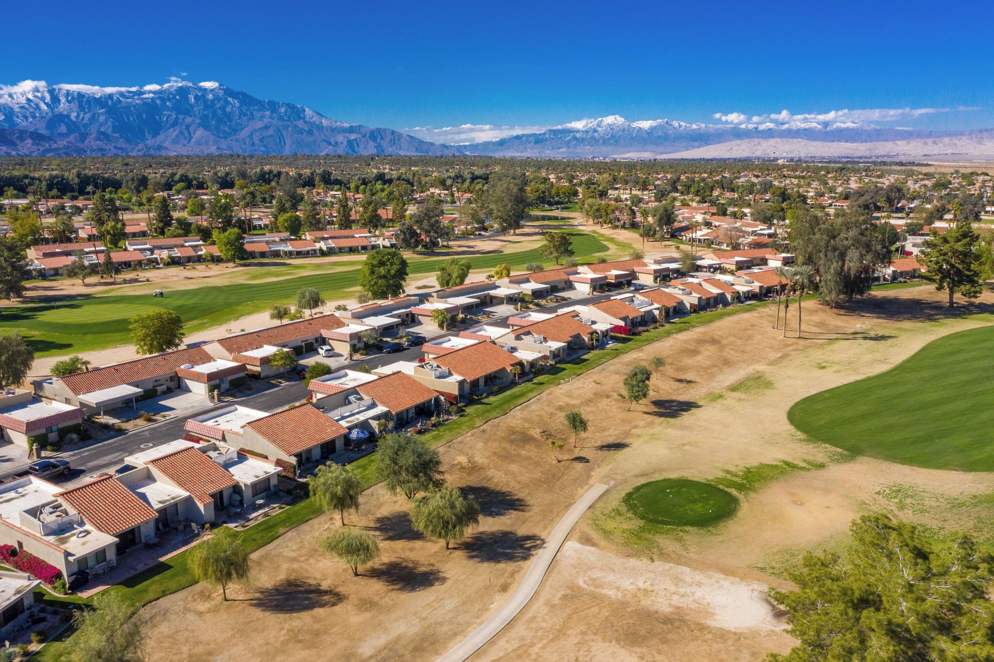 A residential area with houses arranged in rows, a golf course, and mountains in the background.