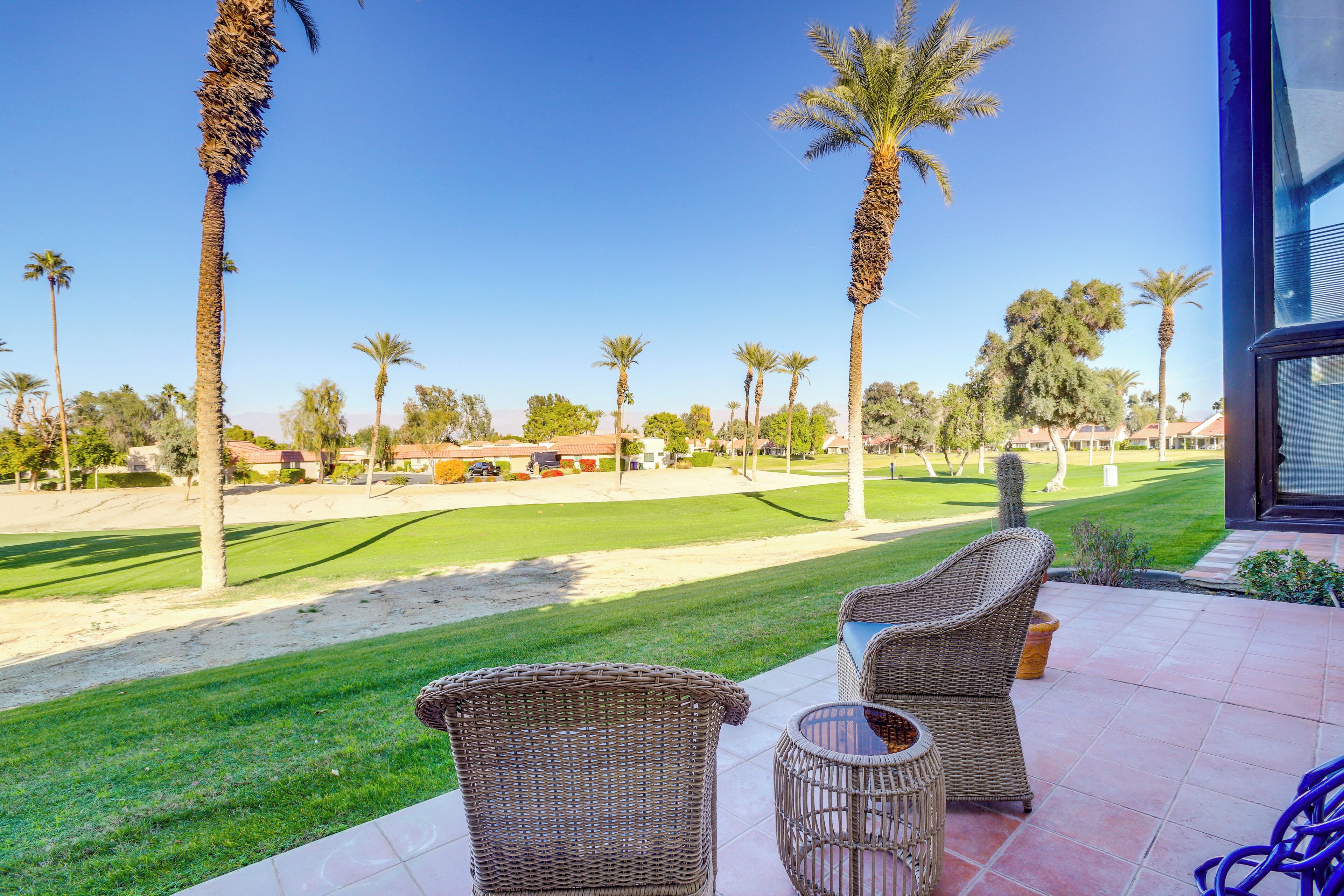 Eine Terrasse mit Korbmöbeln, Blick auf einen Golfplatz und Palmen.