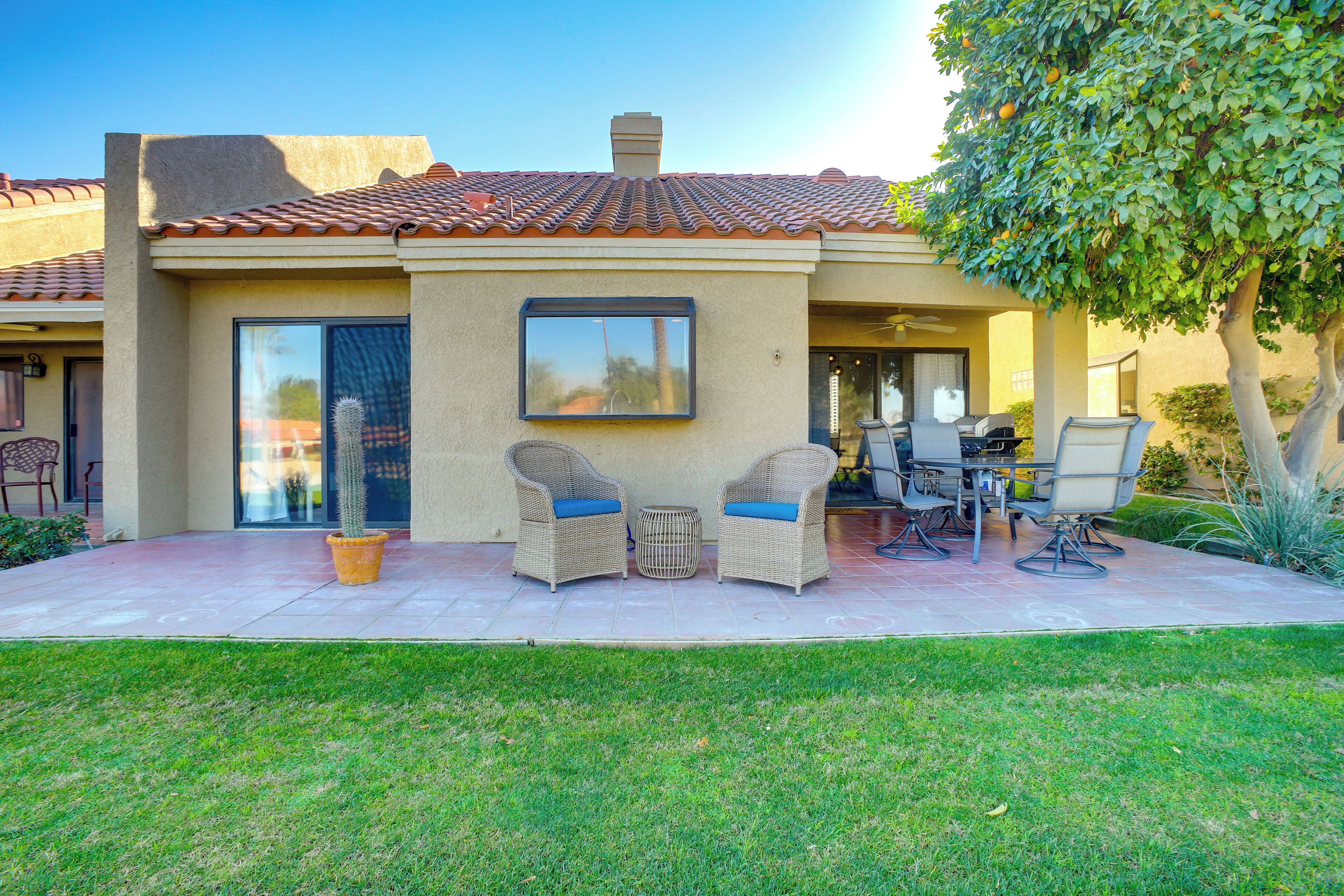 A house with a patio, two wicker chairs with cushions, a table, and a cactus.