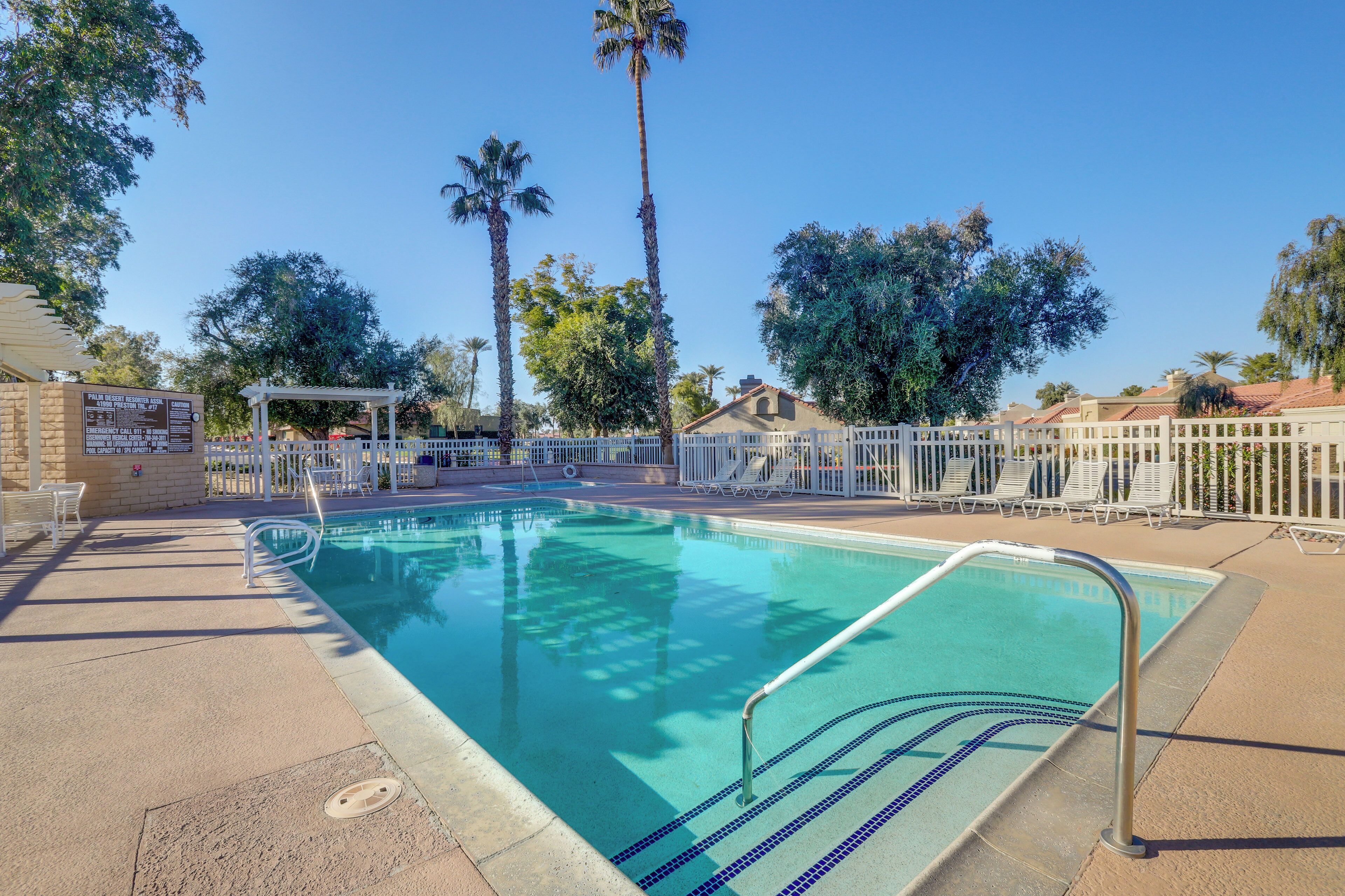 A swimming pool with a white fence, palm trees, and a pergola.