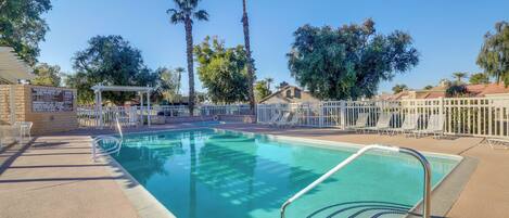 A swimming pool with a white fence, palm trees, and a pergola.