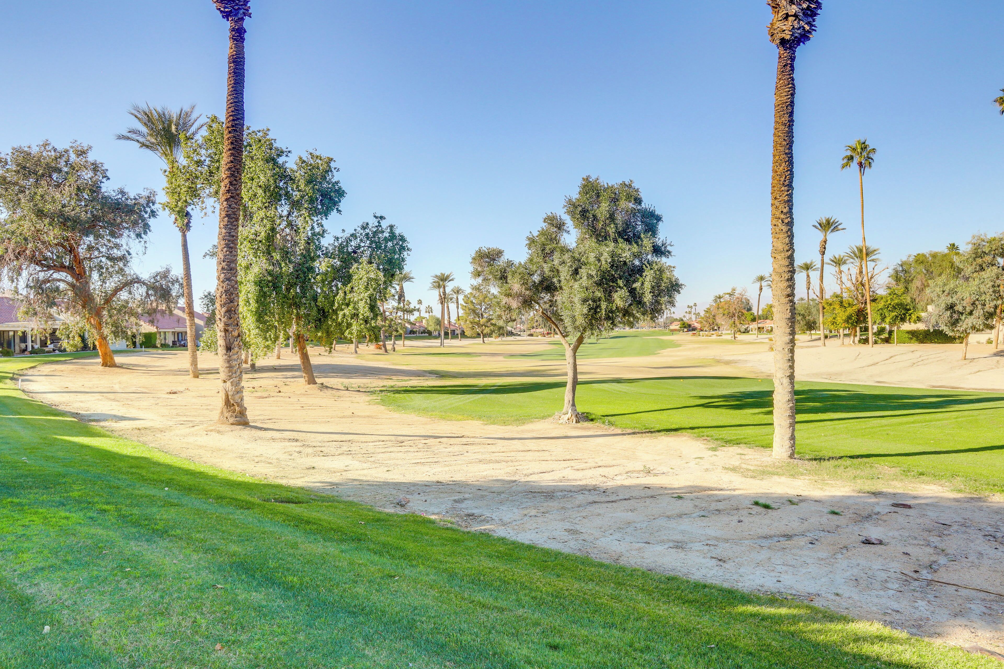 A golf course with sand bunkers, palm trees, and a clear blue sky.
