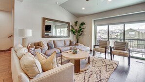 A spacious living room with a large sectional sofa, a round coffee table, and a view of the outdoors through large windows. - Park City Townhome w/ Hot Tub & Mountain Views! (Kamas)