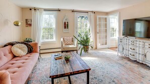 A living room with a pink sofa, a wooden coffee table, a white cabinet, and a television. - Lambertville Retreat - Walk to Shopping & Dining! (Lambertville)