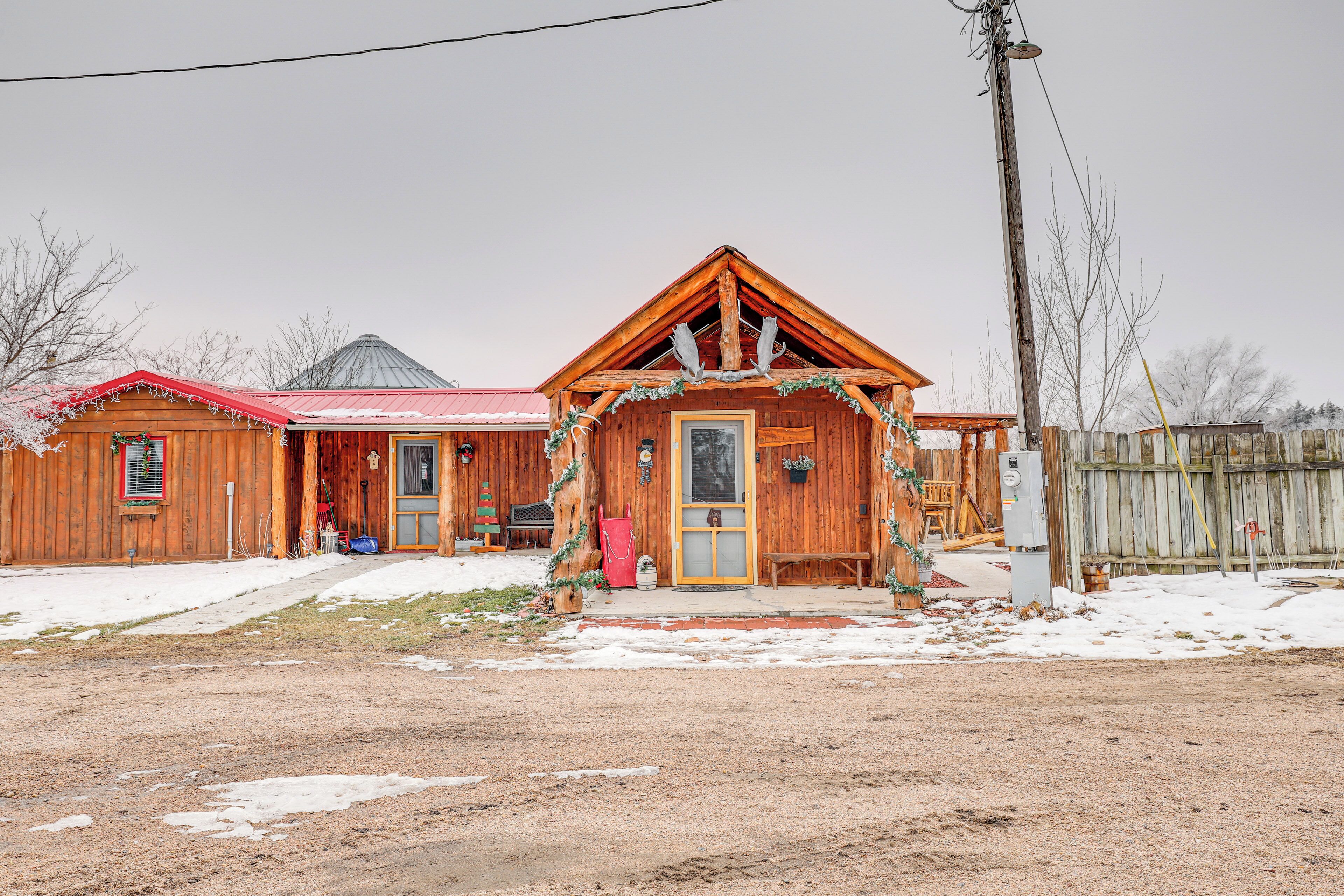 A wooden cabin with a red roof, a front porch, and a snow-covered ground.