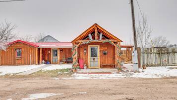 A wooden cabin with a red roof, a front porch, and a snow-covered ground.