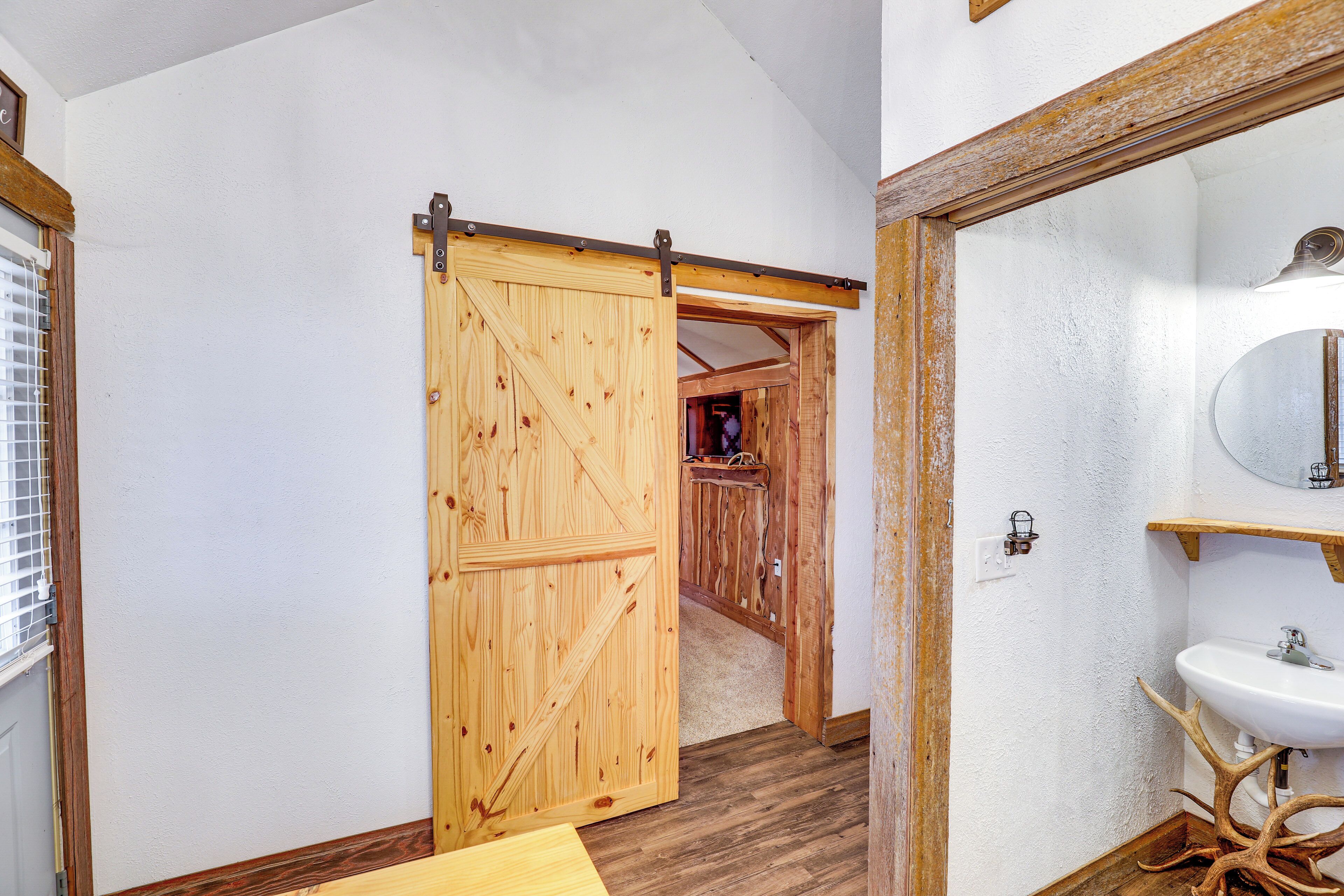 A rustic bathroom with a wooden door, a white sink, and a mirror with a wooden frame.