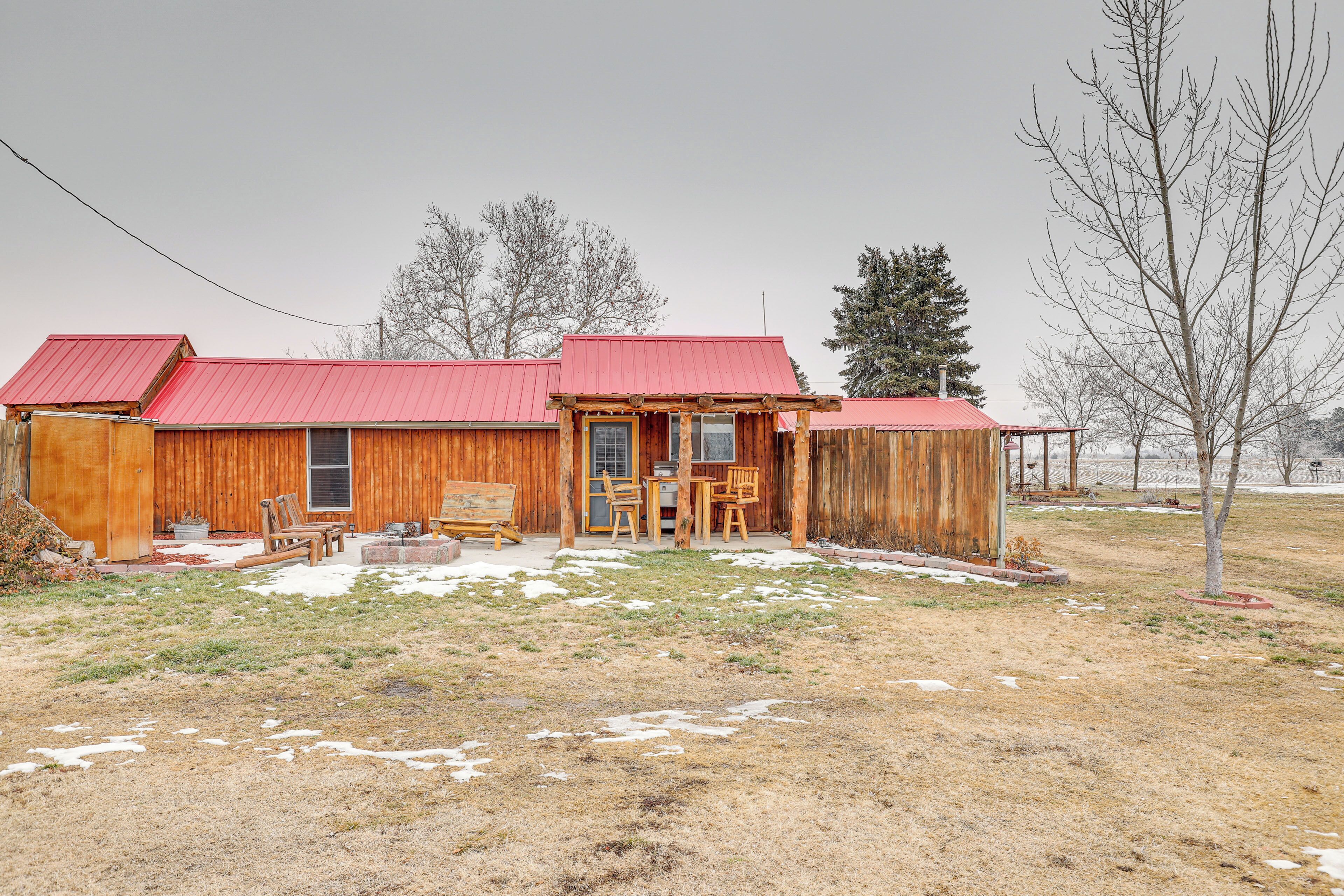 A wooden cabin with a red roof, a porch with chairs, and a small table.