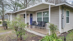 Ein eingeschossiges Haus mit einer Veranda, einer blauen Tür und einer Sitzgelegenheit mit Kissen.