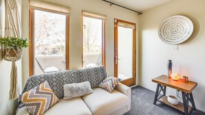 A modern living room with a sofa, patterned cushions, a macrame wall hanging, a round wall decoration, and a small wooden table with a vase and candle. - Bright Santa Fe Condo ~ Half-mi to Meow Wolf! (Santa Fe)