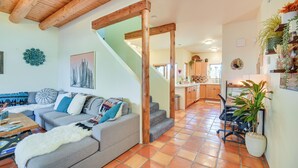 A cozy living room with a grey sofa, wooden beams, a staircase, and a kitchen in the background. - Bright Santa Fe Condo ~ Half-mi to Meow Wolf! (Santa Fe)