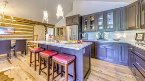 Een moderne keuken met een centraal eiland, barkrukken, houten vloeren en donkere kastjes.