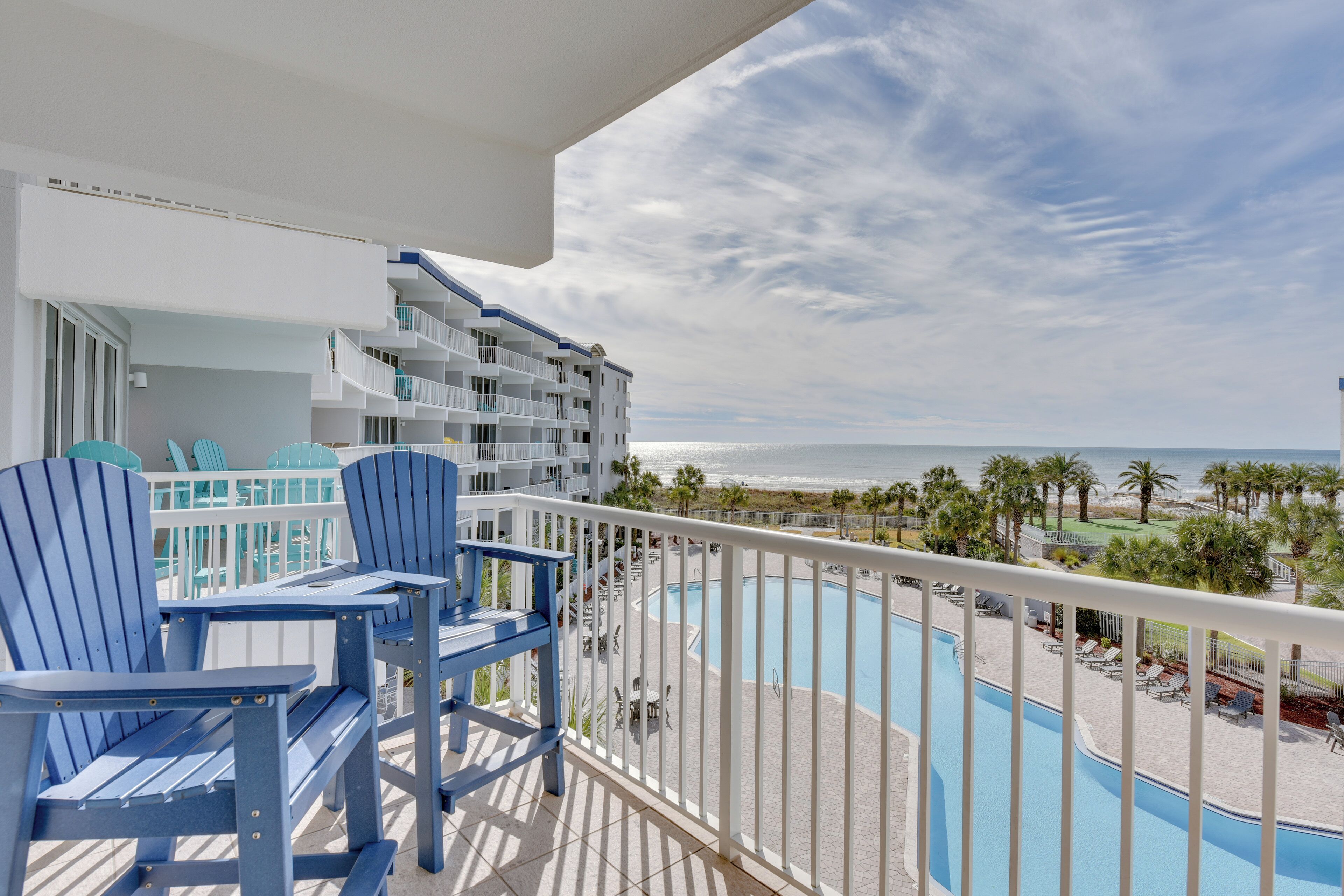 A balcony with blue Adirondack chairs, a pool, and a view of the ocean.