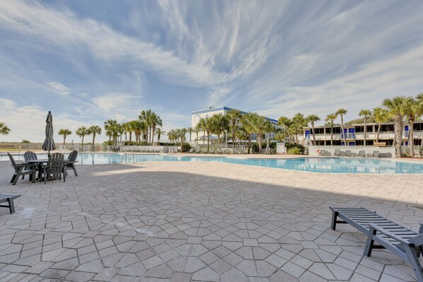 A pool area with hexagonal tiles, lounge chairs, and a building with balconies in the background.