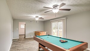 Une table de billard dans une pièce dont le sol est en bois, qui est équipée d’un ventilateur de plafond et possède une fenêtre.