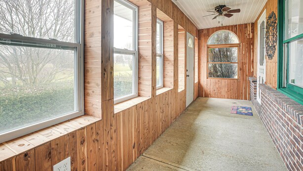 Un couloir aux murs en bois, doté de grandes fenêtres et d’un ventilateur de plafond.