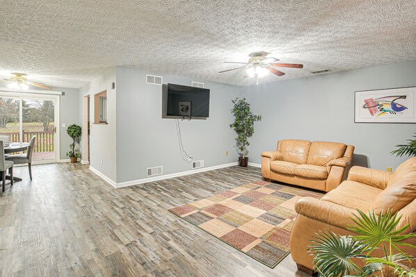 A spacious living room with a wooden floor, a beige leather sofa, a ceiling fan, and a large window. - Spacious Delaware Home w/ Game Room! (Delaware)