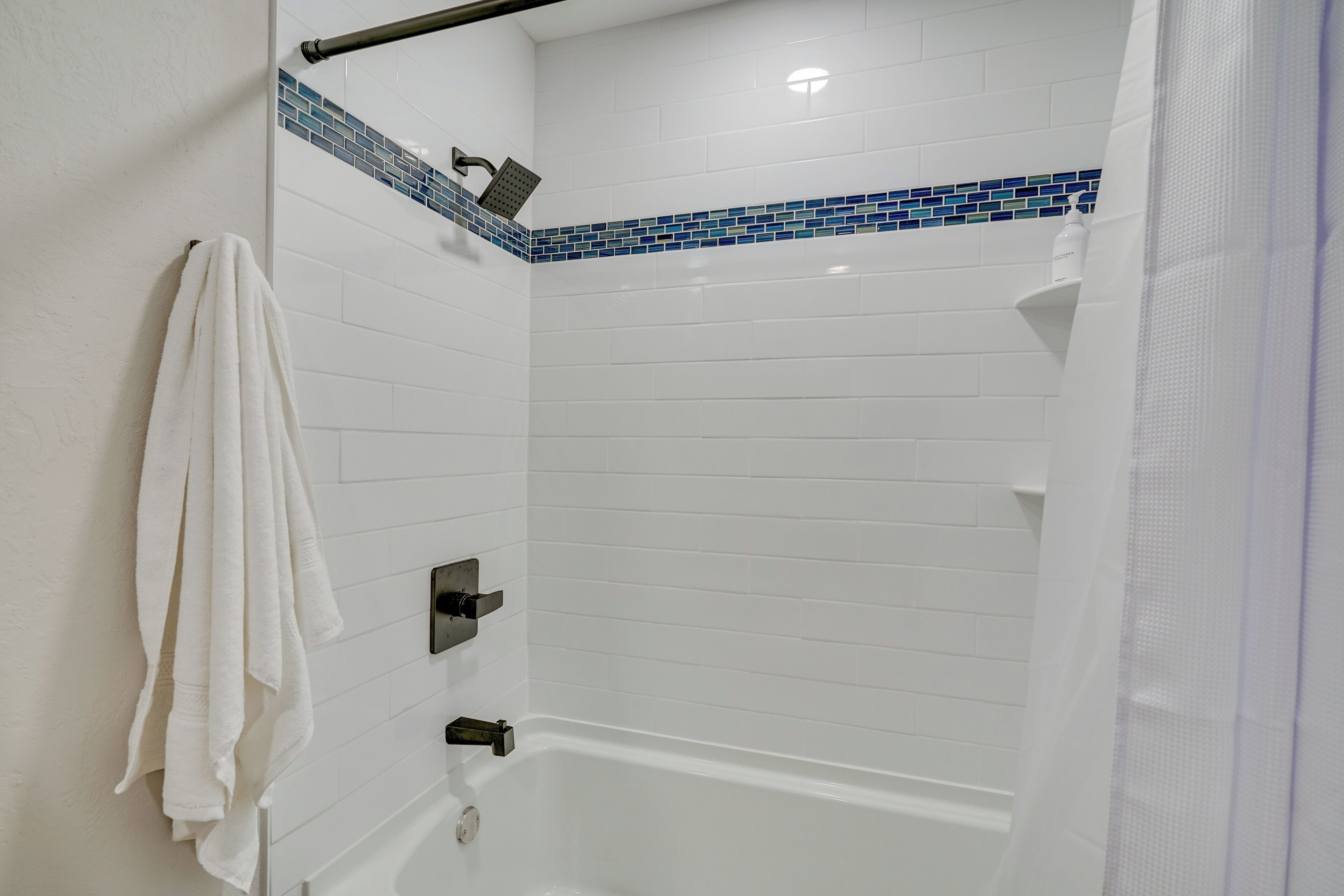 Zona de ducha con paredes de azulejos blancos, un cabezal de ducha y una toalla colgada en la pared.