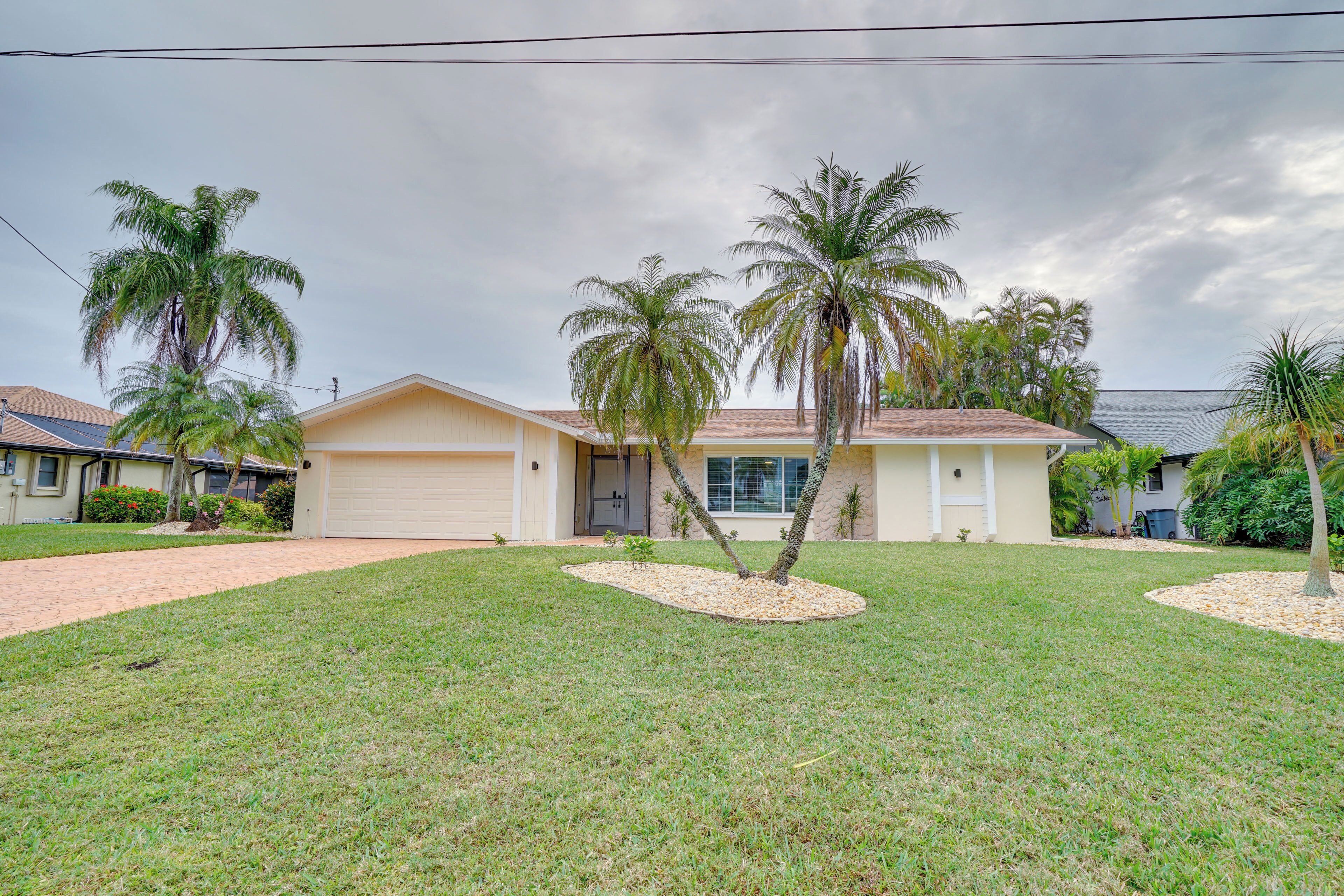 A single-story house with a garage, surrounded by a well-maintained lawn and palm trees.