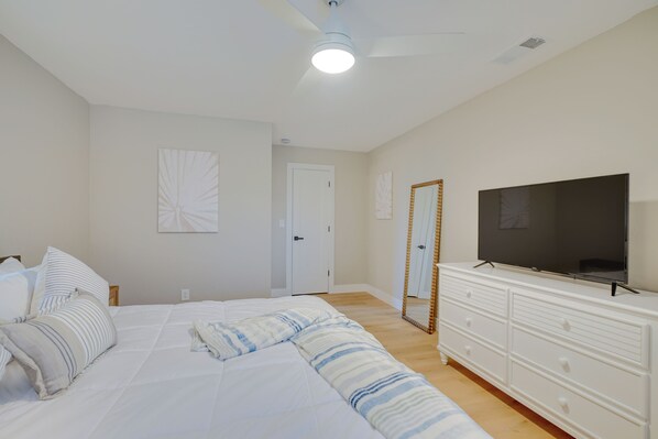 Un dormitorio con cama, televisor, cómoda y ventilador de techo.