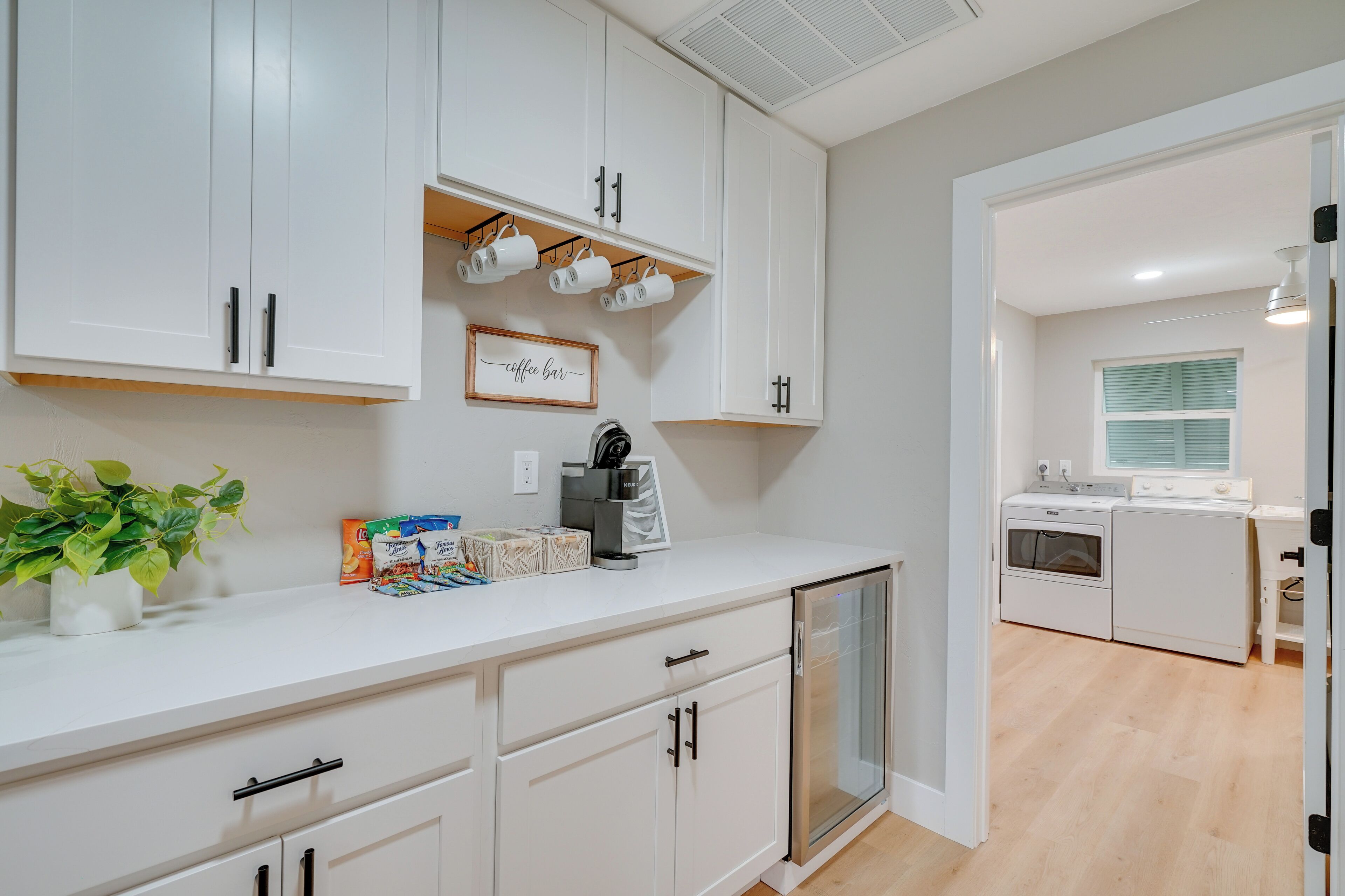 A modern kitchen with white cabinets, a built-in oven, and a coffee bar.