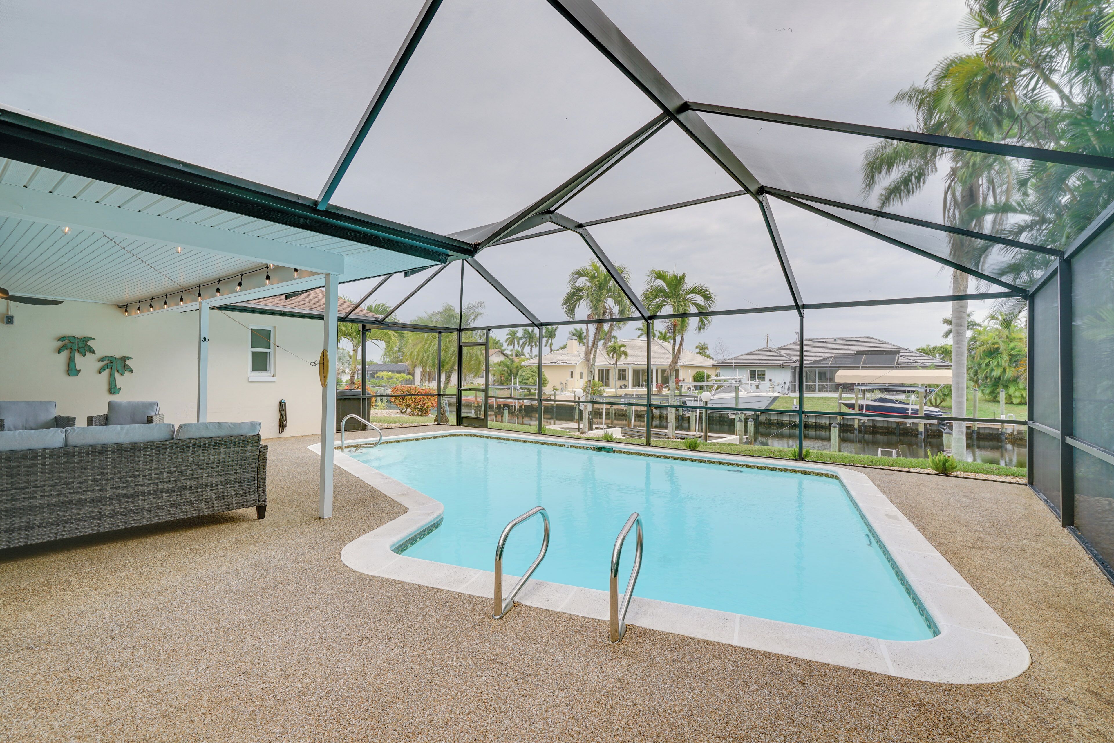 Piscina interna con soffitto in vetro, zona relax con divano e vista su palme e uno specchio d'acqua.