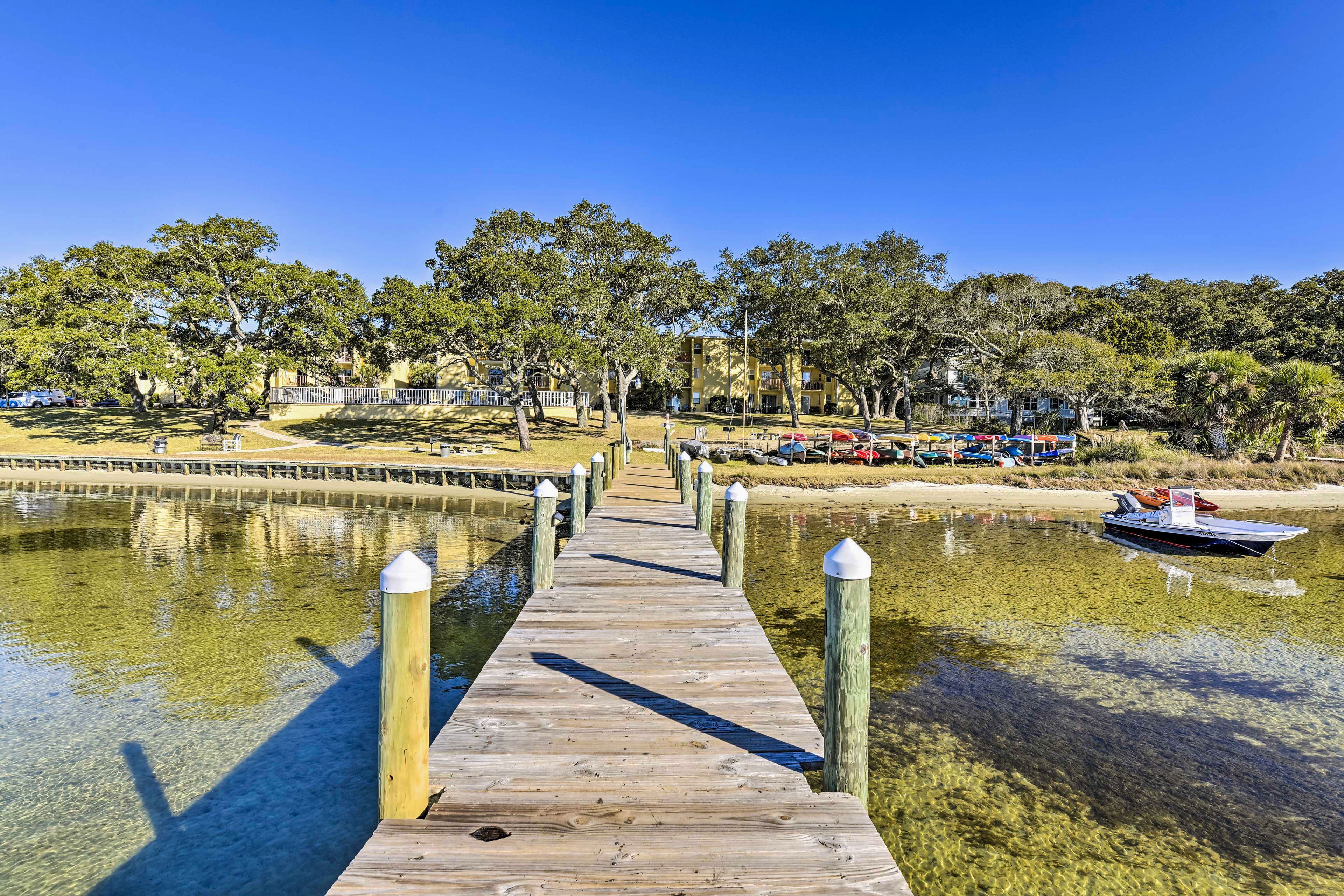 A wooden pier leading to a boat dock, surrounded by trees and a clear sky.