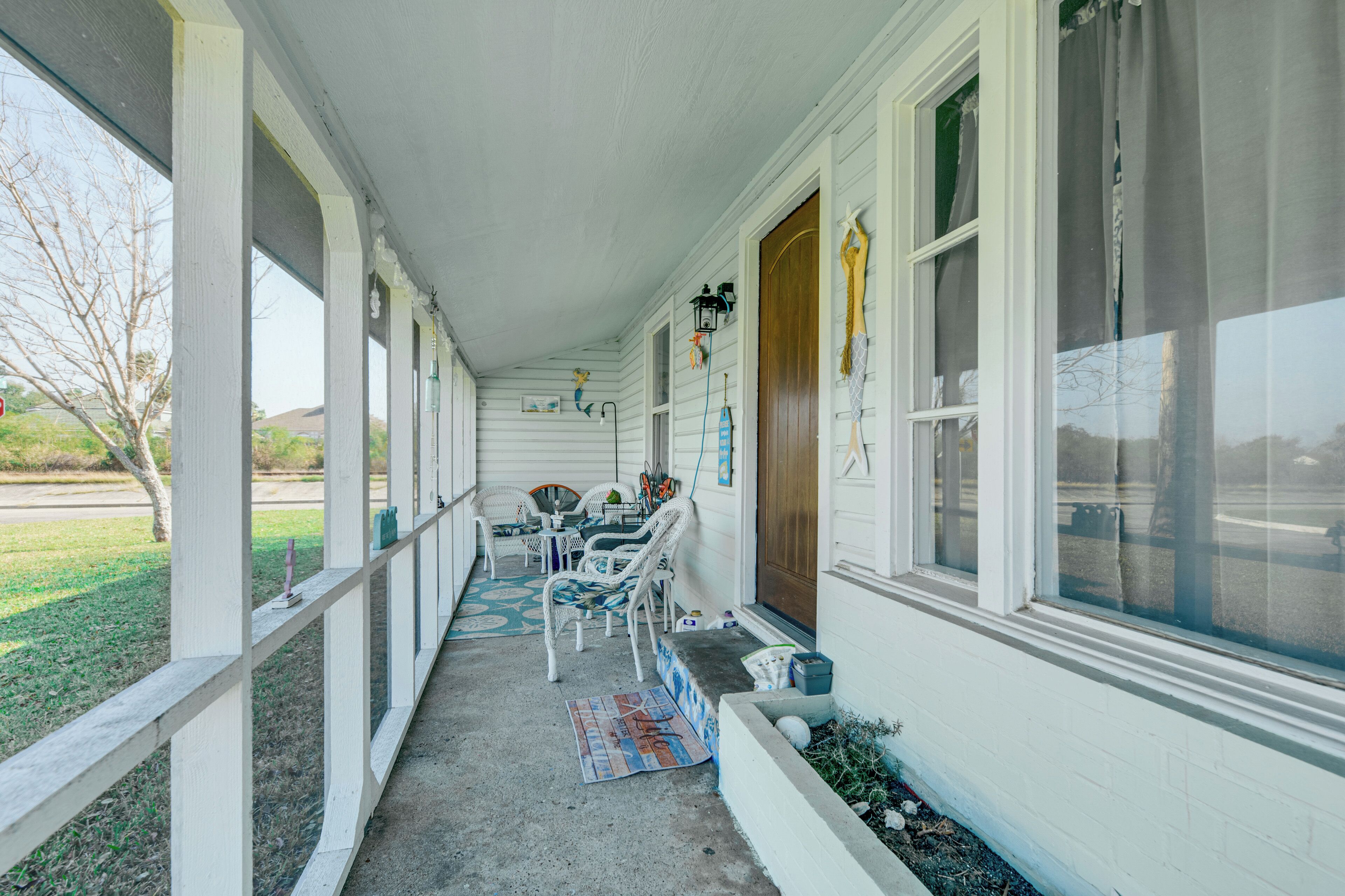 A covered porch with white railings, a wooden door, and a window with curtains.