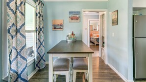A dining area with a table and two chairs, a window with patterned curtains, and a refrigerator.