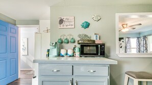 A kitchen with a blue door, a microwave, and teal mugs on the counter.