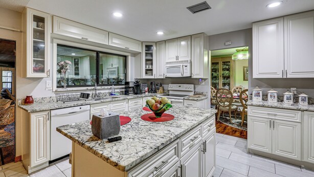 A modern kitchen with white cabinetry, a granite countertop, and a central island. - Tampa Area Home w/ Indoor Pool, Families Welcome! (Brandon)