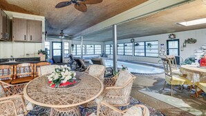 A spacious room with a large round table surrounded by wicker chairs, a ceiling fan, and a view of a swimming pool. - Tampa Area Home w/ Indoor Pool, Families Welcome! (Brandon)