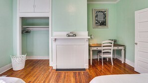 A bedroom with a wooden floor, a white bed, a desk with a chair, a white wardrobe, and a framed picture on the wall. - Sumter Vacation Rental in Historic District! (Sumter)