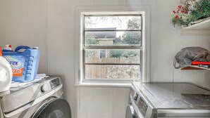 A laundry room with a washing machine, a dryer, and a window with a view of a wooden fence and trees. - Sumter Vacation Rental in Historic District! (Sumter)