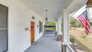 A covered porch with a swing, a brick planter, and an American flag. - Sumter Vacation Rental in Historic District! (Sumter)