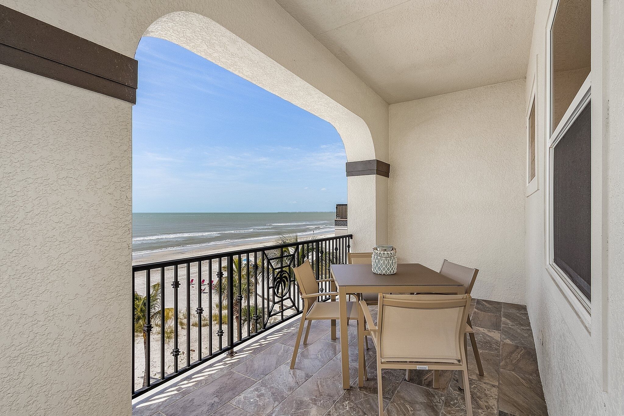 Un balcon avec vue sur la plage, une table avec des chaises et une fenêtre.